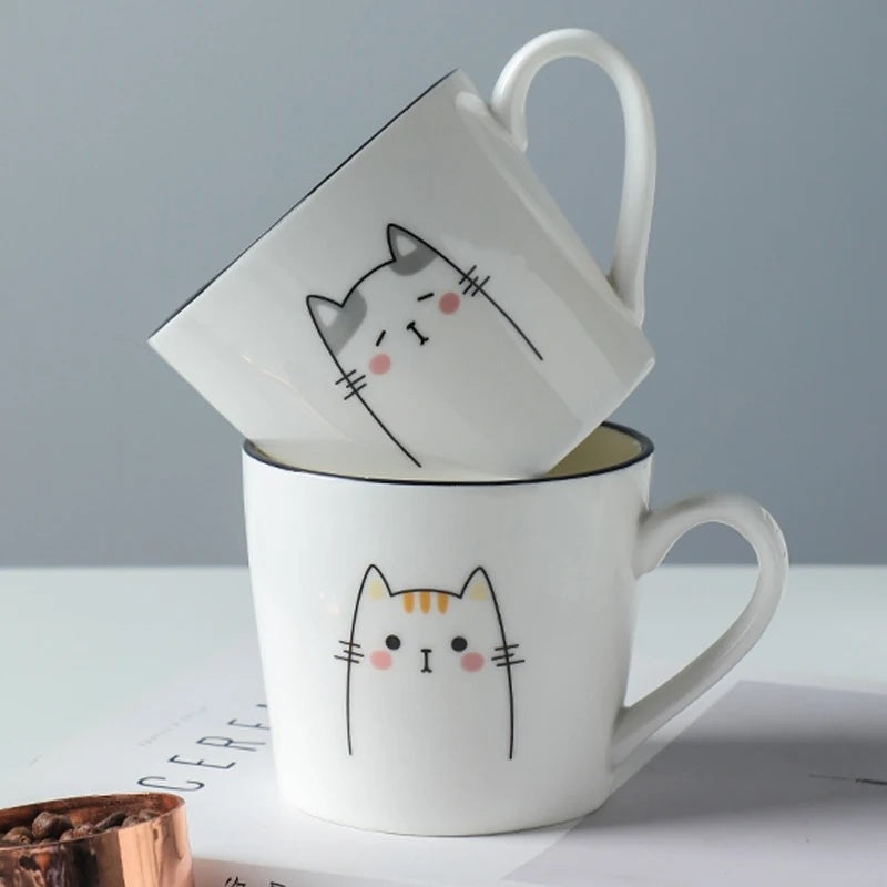 Two cat-themed mugs stacked on a light surface with a gray background