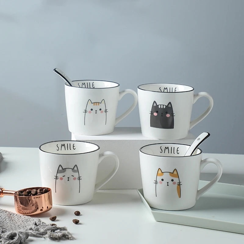 Set of four white mugs with cat illustrations and 'SMILE' text on a light gray background.