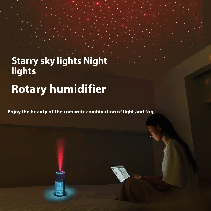 Person using a laptop under a starry light projection device in a dark room.