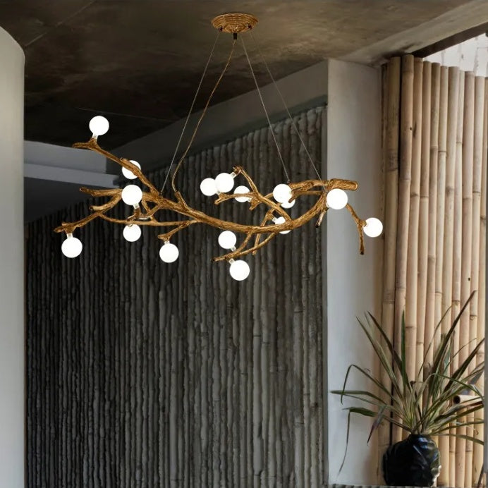 Branch-like chandelier with white lights hanging in a room with a textured wall and plant.